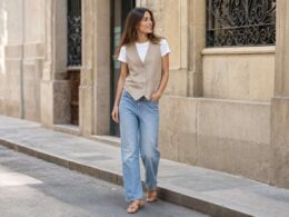 Mujer con chaleco sastre beige, camiseta blanca y vaqueros en una calle luminosa.