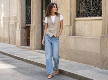 Mujer con chaleco sastre beige, camiseta blanca y vaqueros en una calle luminosa.