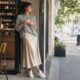 Mujer con falda satinada champán, jersey gris y zapatillas blancas en una cafetería.